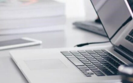 open laptop on desk with phone and books